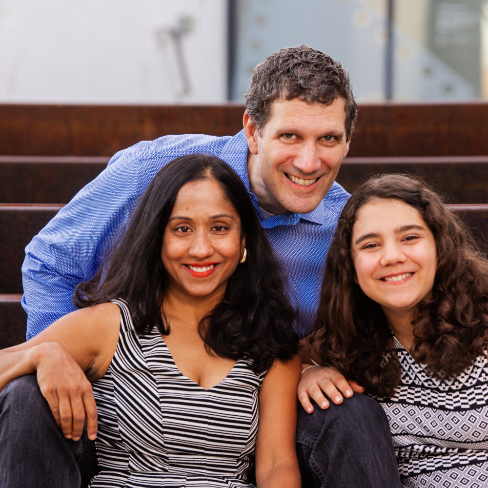Founder, Gita Chakrabarti, of gutBFF with her family of three sitting together on steps outdoors.