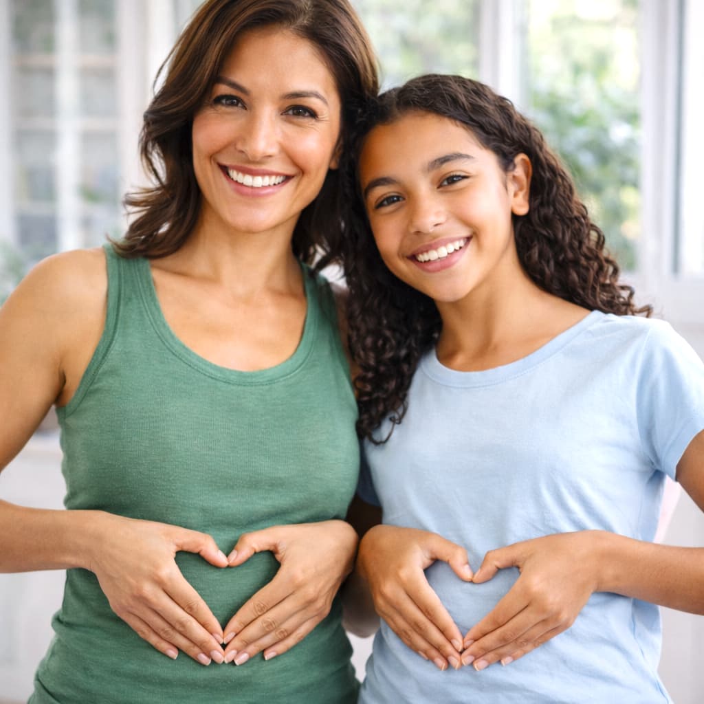 Woman and young girl making heart shapes with their hands over their stomachs, smiling.